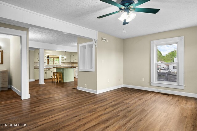 unfurnished living room featuring a textured ceiling, a ceiling fan, baseboards, and dark wood-type flooring
