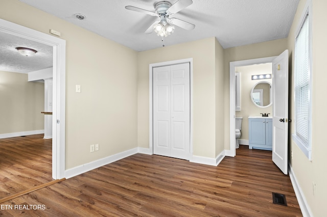 unfurnished bedroom featuring a closet, visible vents, baseboards, a textured ceiling, and wood finished floors
