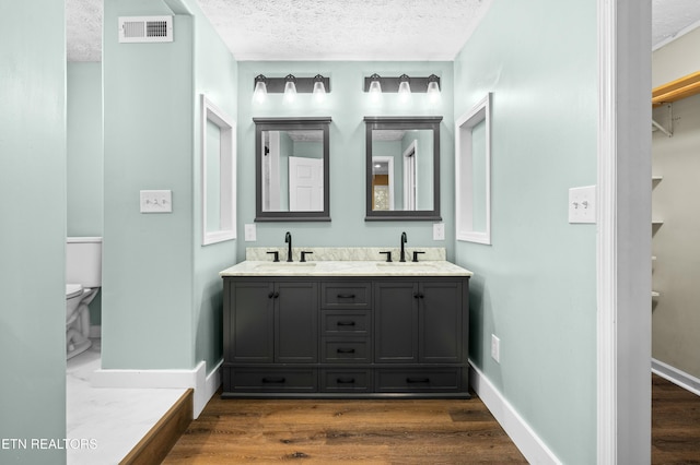 full bathroom with visible vents, toilet, a textured ceiling, and a sink