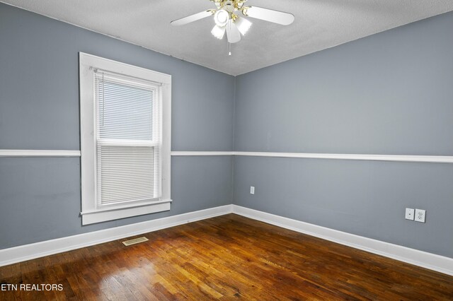 empty room with wood finished floors, visible vents, ceiling fan, and baseboards