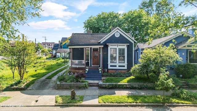 bungalow-style home with driveway, covered porch, and a chimney