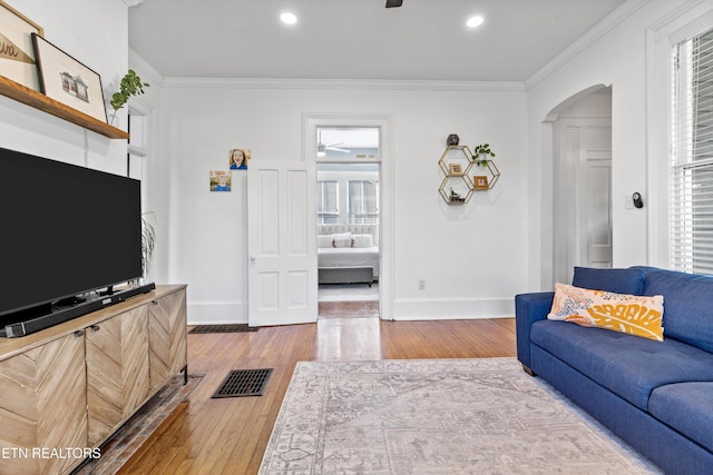 living room featuring a ceiling fan, crown molding, arched walkways, hardwood / wood-style flooring, and baseboards