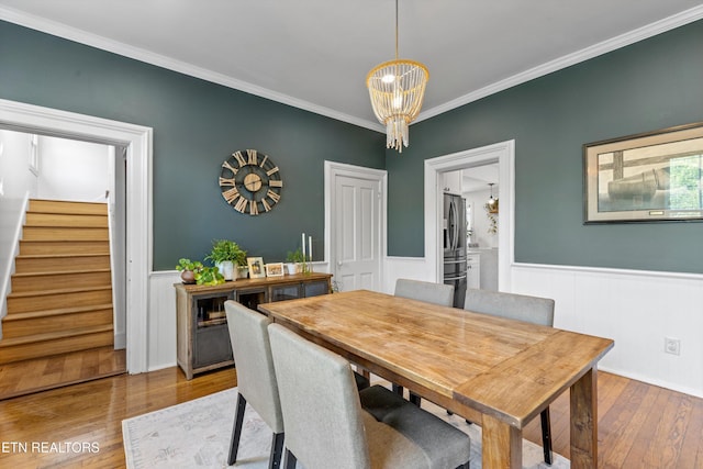 dining area featuring stairs, a notable chandelier, hardwood / wood-style floors, and a wainscoted wall