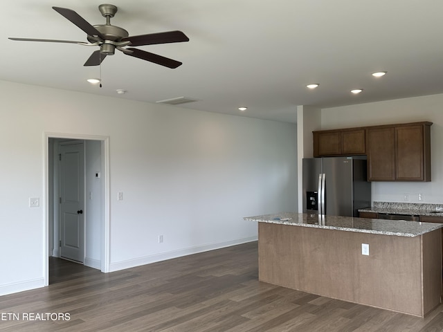 kitchen featuring visible vents, a kitchen island, dark wood-style flooring, light stone countertops, and stainless steel fridge with ice dispenser