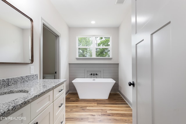 full bathroom with recessed lighting, vanity, a freestanding bath, visible vents, and wood finished floors