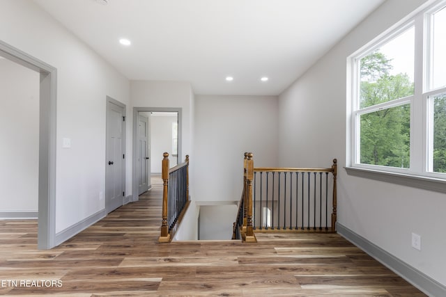 hall with wood finished floors, a wealth of natural light, and an upstairs landing