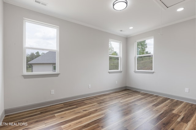 empty room with attic access, visible vents, baseboards, ornamental molding, and wood finished floors