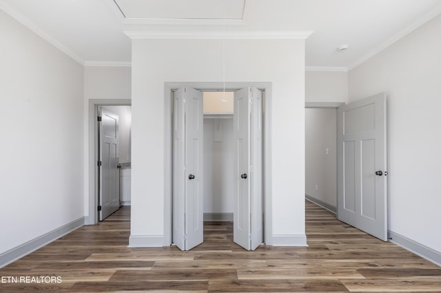 unfurnished bedroom with crown molding, baseboards, a closet, attic access, and wood finished floors
