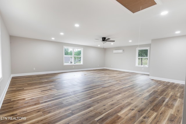 empty room with attic access, a wall mounted air conditioner, wood finished floors, and plenty of natural light