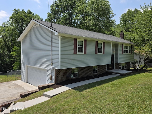 raised ranch featuring fence, an attached garage, a shingled roof, a front lawn, and concrete driveway