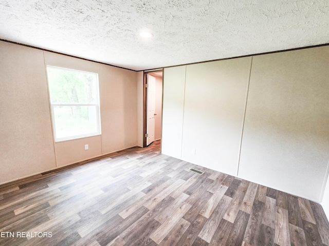 unfurnished room featuring visible vents, wood finished floors, and a textured ceiling