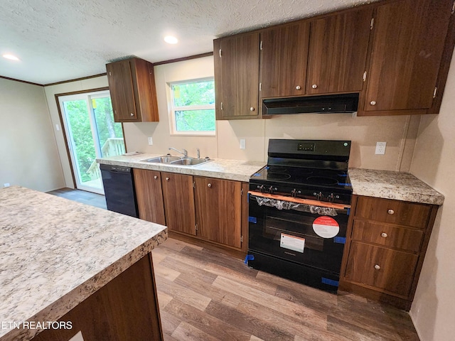 kitchen featuring light wood-style floors, under cabinet range hood, black appliances, a sink, and a textured ceiling