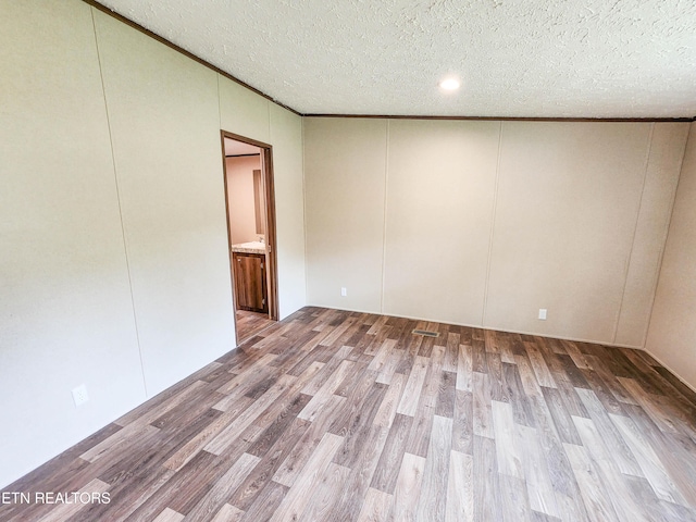 spare room featuring ornamental molding, a textured ceiling, a decorative wall, and wood finished floors