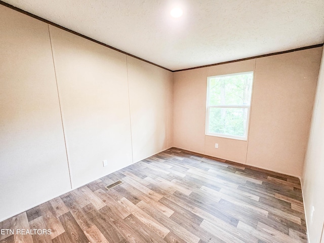 empty room with ornamental molding, a textured ceiling, visible vents, and light wood finished floors