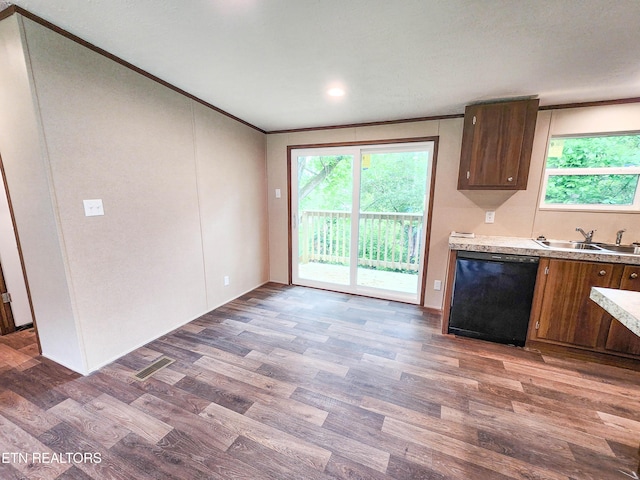 kitchen with a sink, black dishwasher, light countertops, ornamental molding, and wood finished floors