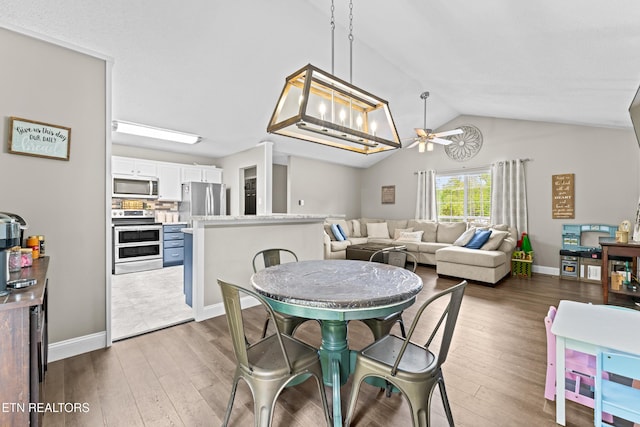 dining space with ceiling fan, vaulted ceiling, wood finished floors, and baseboards