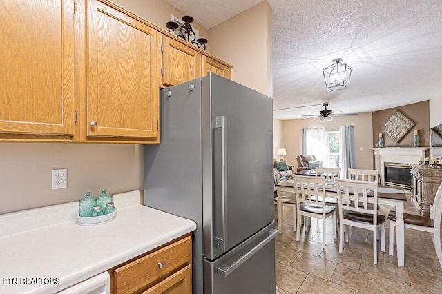 kitchen featuring light countertops, freestanding refrigerator, open floor plan, a glass covered fireplace, and a ceiling fan