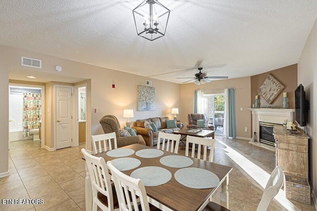 dining space featuring a textured ceiling, visible vents, ceiling fan, a glass covered fireplace, and light tile patterned flooring