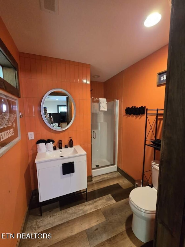 bathroom with wood finished floors, toilet, vanity, visible vents, and a stall shower