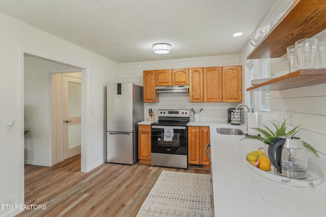 kitchen featuring a sink, stainless steel appliances, light wood-style floors, under cabinet range hood, and light countertops