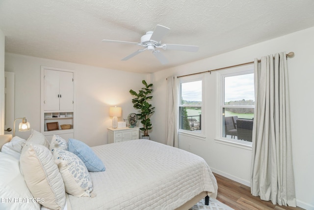 bedroom featuring a ceiling fan, baseboards, a textured ceiling, and light wood-type flooring