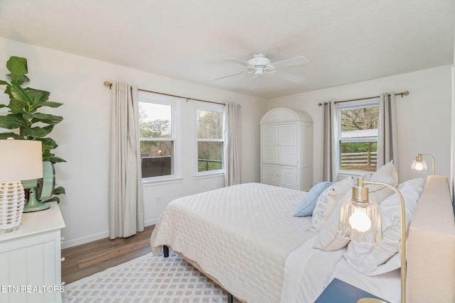bedroom featuring baseboards, wood finished floors, ceiling fan, and multiple windows