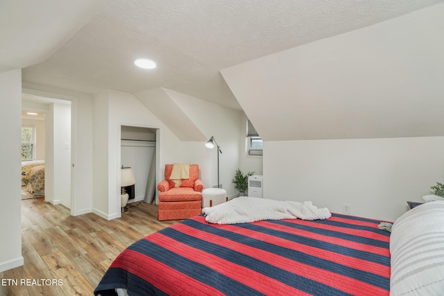 bedroom featuring recessed lighting, light wood-style floors, baseboards, a textured ceiling, and lofted ceiling