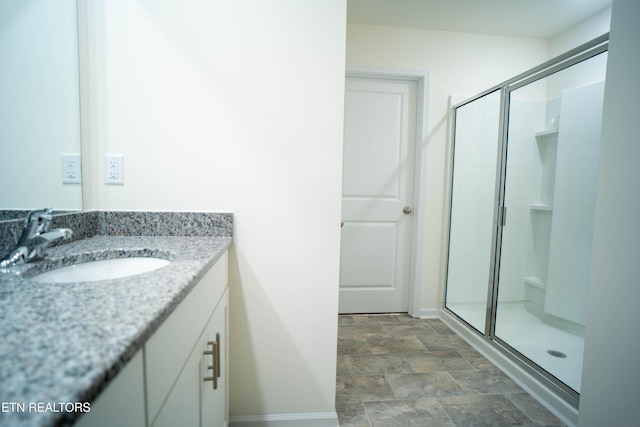 bathroom featuring baseboards, stone finish flooring, a shower stall, and vanity