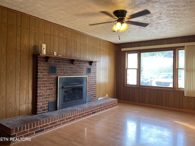 unfurnished living room featuring a fireplace, a textured ceiling, baseboards, and wooden walls