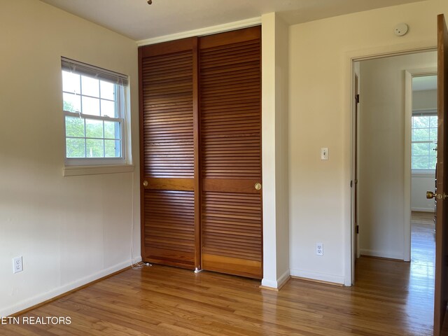 unfurnished bedroom featuring light wood-style flooring, a closet, and multiple windows