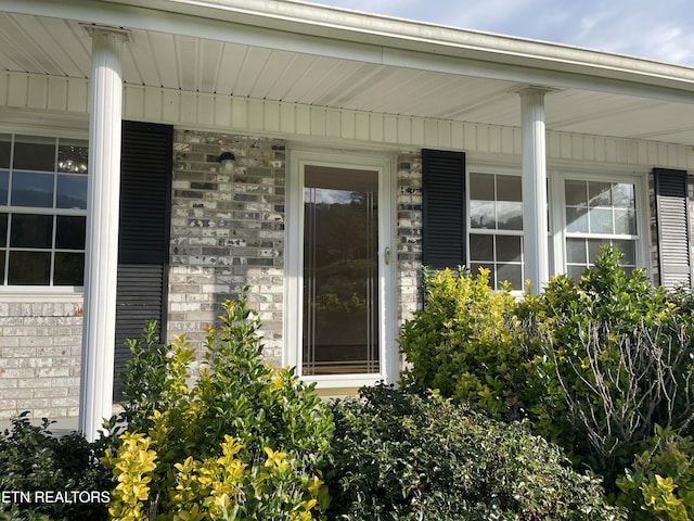 property entrance featuring a porch and brick siding