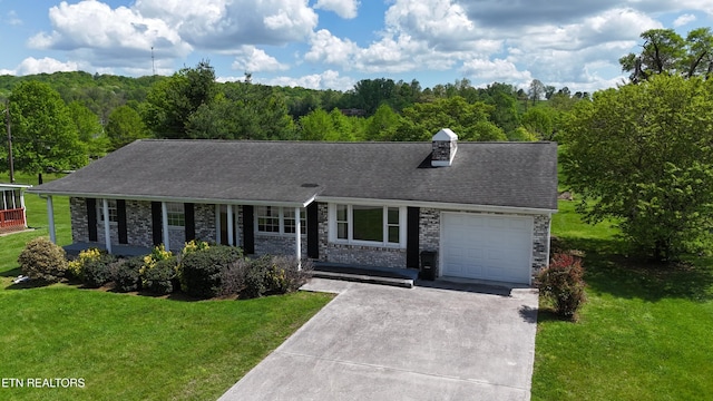 ranch-style house featuring covered porch, a garage, driveway, a front yard, and a forest view