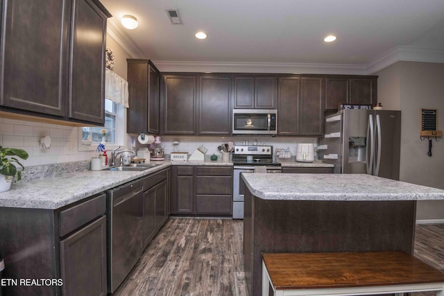 kitchen with appliances with stainless steel finishes, a sink, dark brown cabinets, dark wood-style floors, and crown molding
