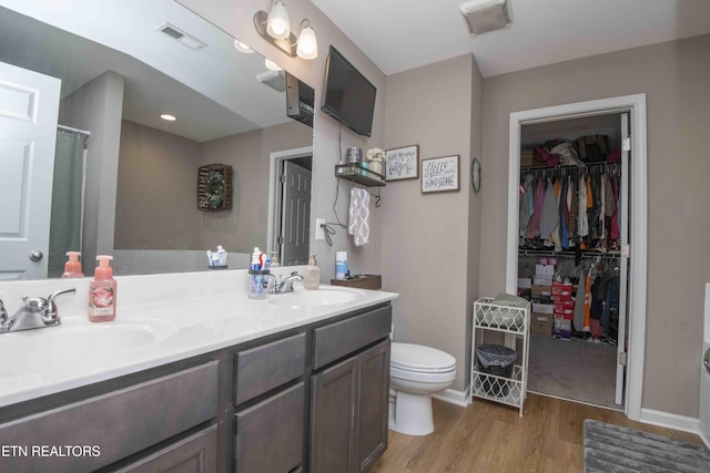 bathroom with wood finished floors, toilet, double vanity, a spacious closet, and a shower