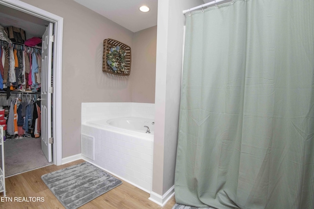 full bath featuring a garden tub, wood finished floors, a walk in closet, and baseboards