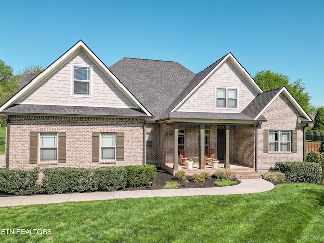 craftsman-style home featuring roof with shingles, a front lawn, covered porch, and brick siding