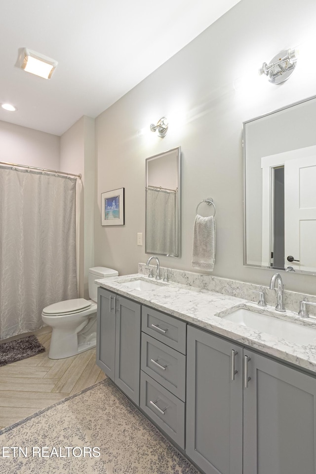 bathroom with toilet, double vanity, and a sink