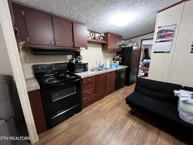 kitchen featuring under cabinet range hood, light countertops, black appliances, a sink, and light wood-type flooring