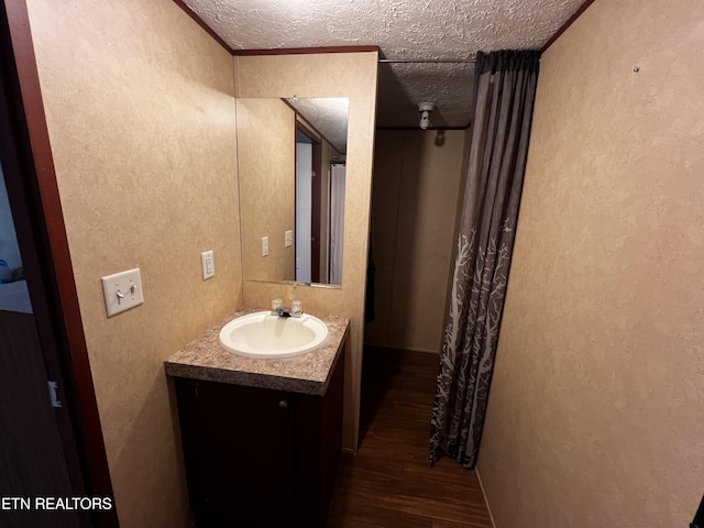 bathroom featuring vanity, a textured ceiling, a textured wall, and wood finished floors