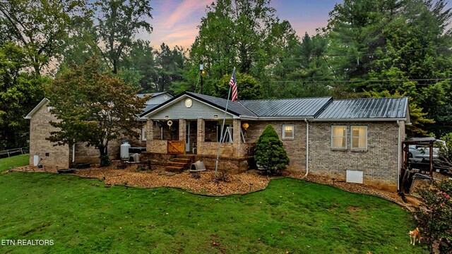 single story home with covered porch, brick siding, a front lawn, and metal roof