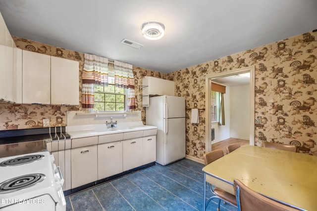 kitchen featuring visible vents, white appliances, wallpapered walls, white cabinets, and dark tile patterned flooring