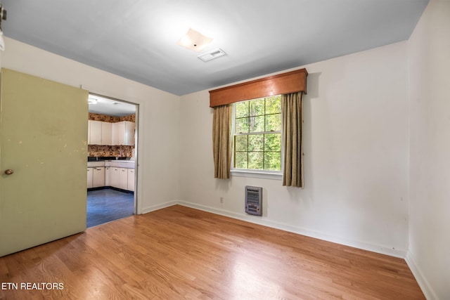 unfurnished room featuring baseboards, heating unit, and wood finished floors
