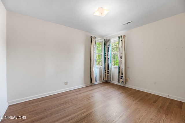 unfurnished room featuring baseboards, visible vents, and wood finished floors