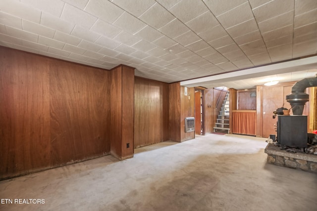 finished below grade area featuring carpet floors, a wood stove, wood walls, and stairway