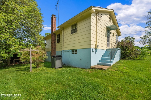 back of property featuring a yard, central AC unit, and a chimney