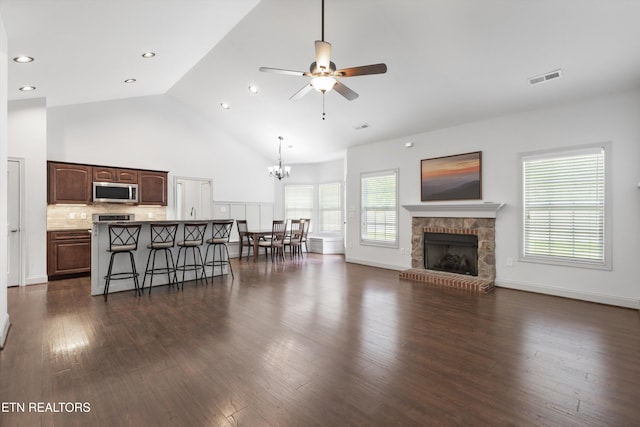 living area with visible vents, a fireplace, dark wood finished floors, high vaulted ceiling, and ceiling fan with notable chandelier