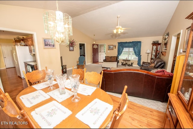 dining room with ceiling fan with notable chandelier, vaulted ceiling, and light wood-style floors