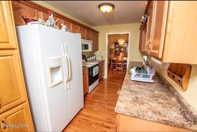 kitchen with light wood-type flooring, white appliances, a textured ceiling, and light stone counters