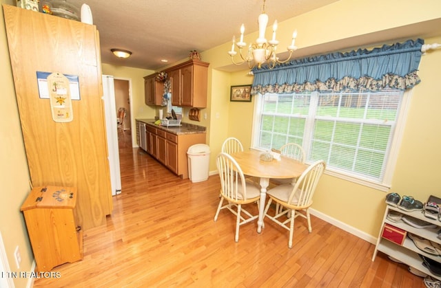dining area with an inviting chandelier, a textured ceiling, light wood-style floors, and baseboards
