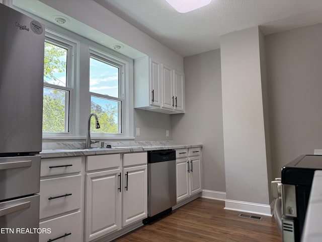 kitchen featuring white cabinets, a sink, appliances with stainless steel finishes, baseboards, and dark wood finished floors